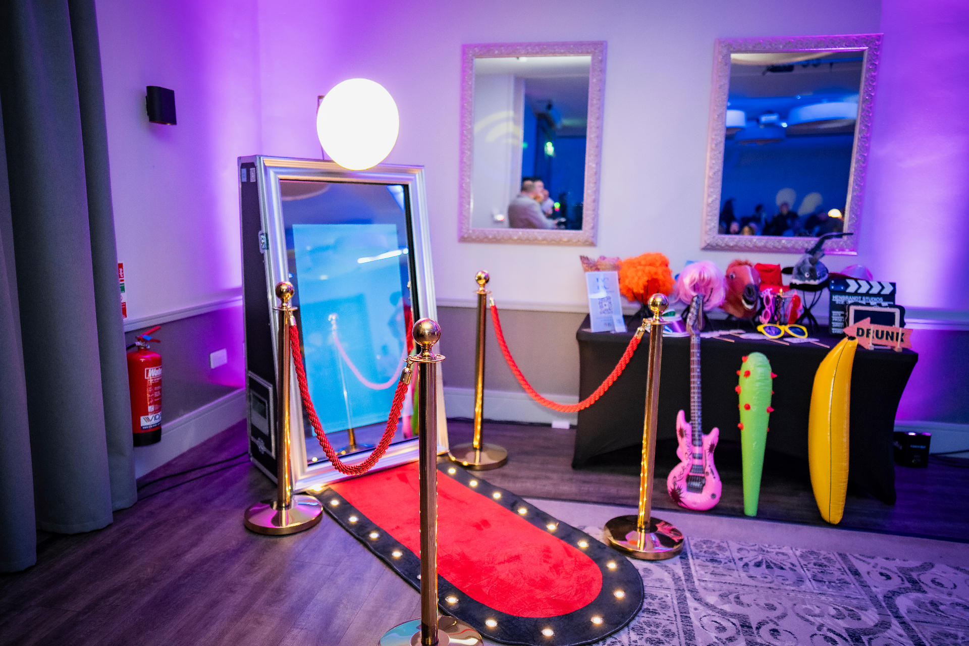 Our silver-framed mirror booth with red carpet, gold posts and neon 'Touch to take a selfie' prompt